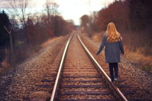 Woman with red hair, back to the camera, walking tandem on the right of the train tracks.