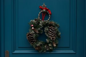 Pine tree wreathe with a red bow and a pinecone on the right side, hung on a dark blue door.