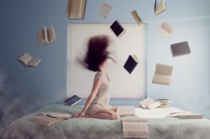 Photo of blurry, brunette woman, with books flying around her in the air.