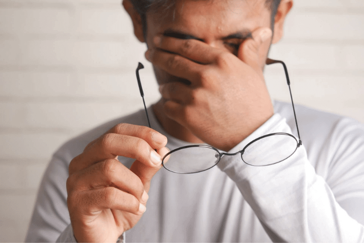 man rubbing his eyes holding his glasses with one hand