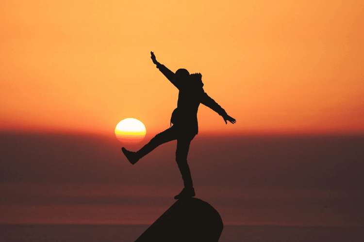 silhouette of man balancing on top of rock at sunset