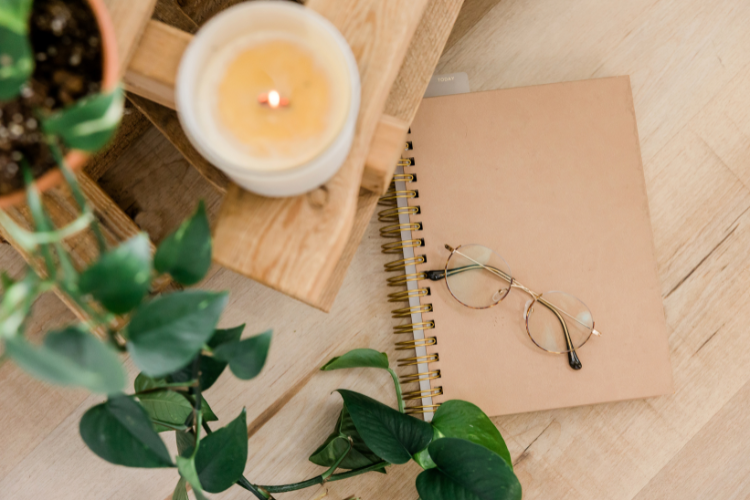 decorative items surrounding a candle, notebook, and glasses