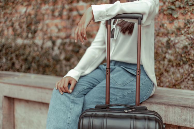 woman sitting on a wall leaning on a suitcase handle