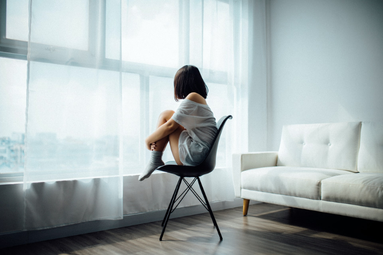 Woman being affected by hormones sitting in chair and staring out window