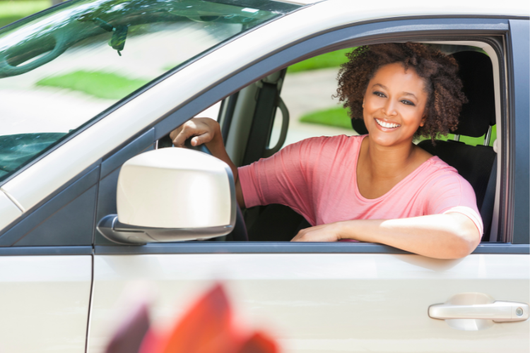 darker skinned woman with a pink shirt smiling from inside her white car, she has recovered from being dizzy while driving